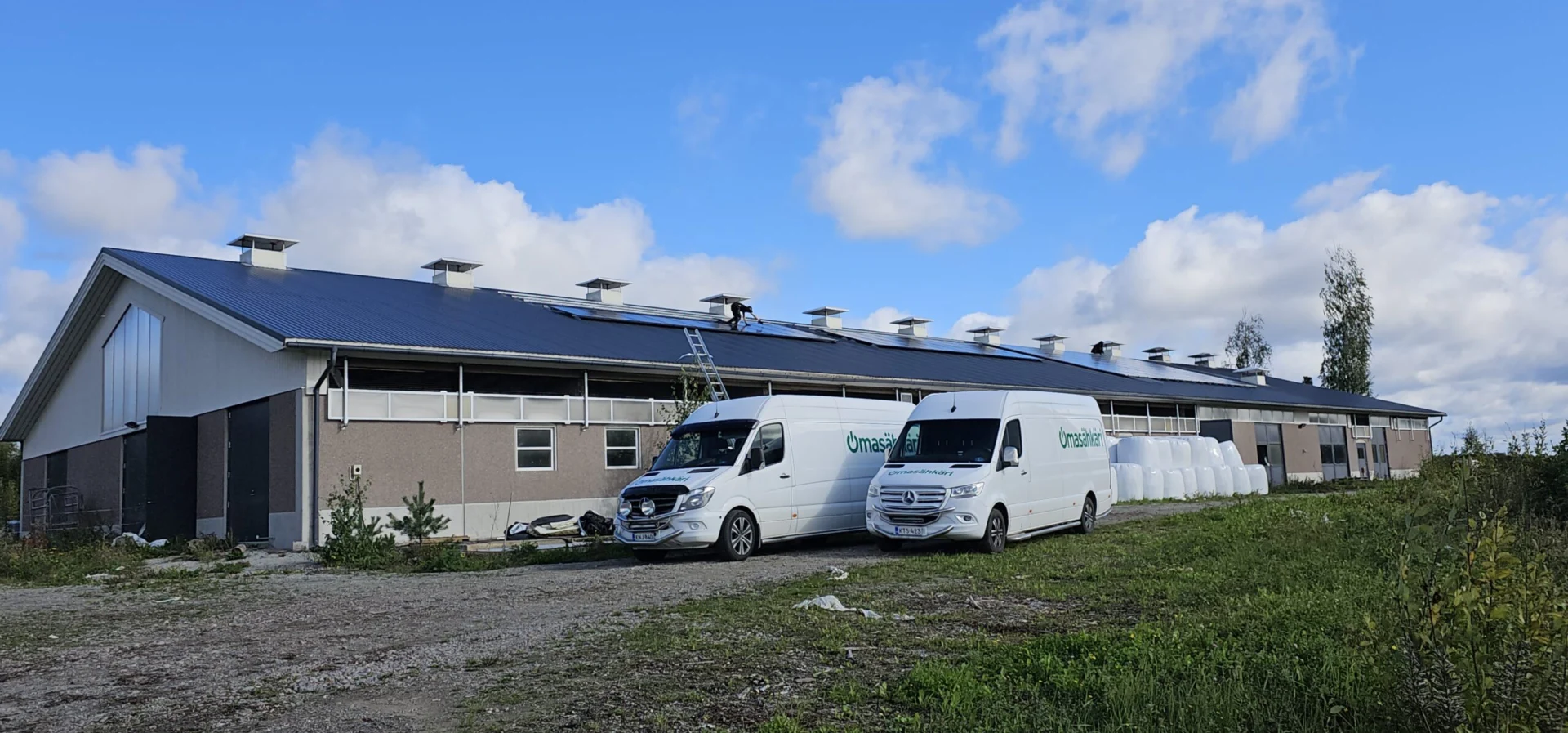 Omasähkärin asennusautot hallirakennuksen pihalla, katolla aurinkopaneelit